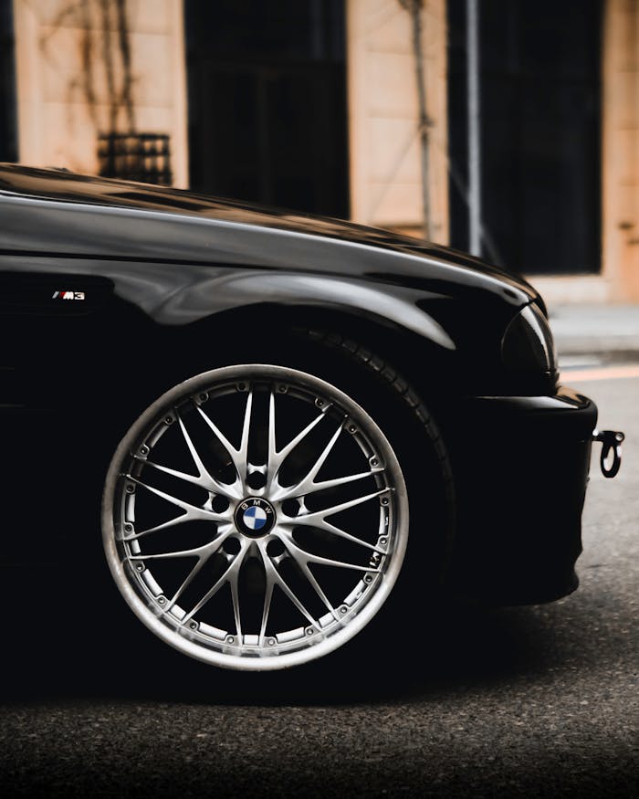 Close-up of a luxury sports car wheel with shiny chrome alloy rim in an urban setting.